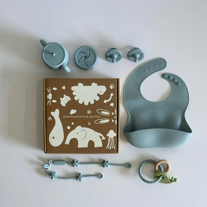 “First daycare set including silicone bib, straw cup, two snack cups, teether ring, and pacifier clips, displayed with gift box.”