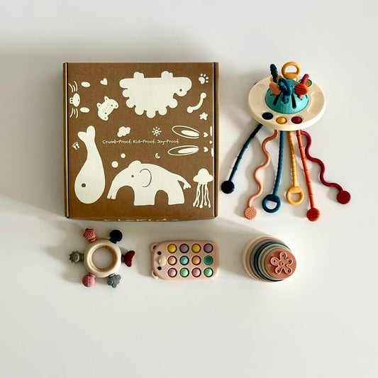 “Baby sensory toy gift set with five silicone Montessori-inspired toys, including pull-string toy, stackable cups, pop-it, teether, and rattle, displayed with eco-friendly gift box.”
